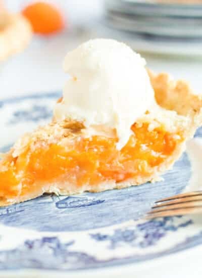 Slice of apricot pie topped with scoop of vanilla ice cream on a dessert plate.