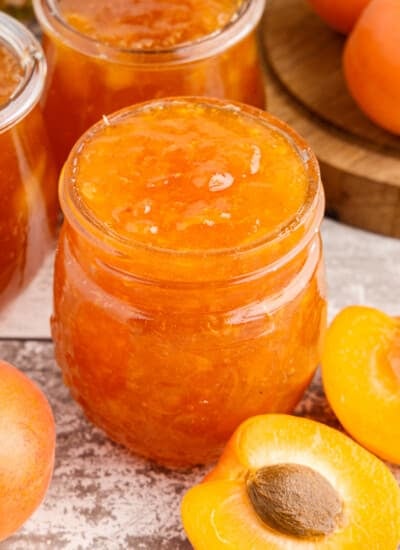 Close up of Apricot Pineapple Jam in glass jars, fresh apricots on a wooden countertop.