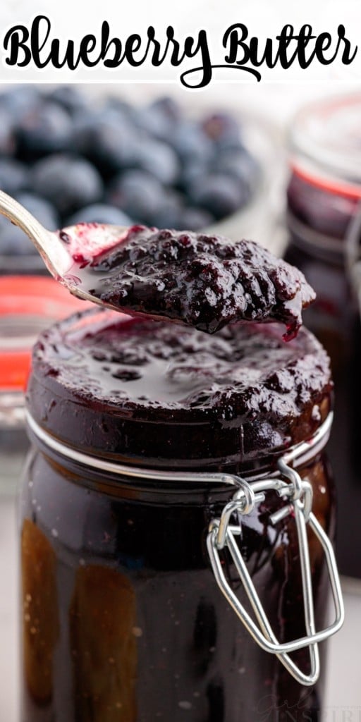 Close up of Blueberry Butter in a mason jar with a metal spoon scooping out the butter and blueberries in a bowl in the background