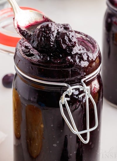 A mason jar filled with Blueberry Butter, a spoon lifting some out.