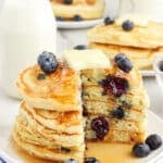 A stack of 6 blueberry buttermilk pancakes topped with butter with a bite taken out.