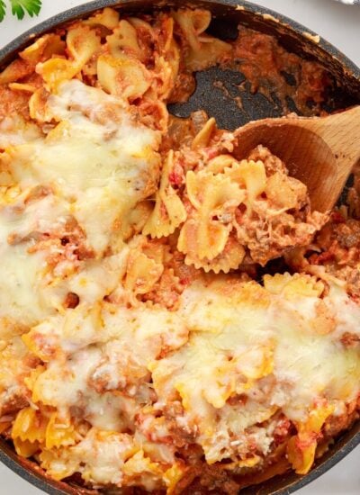 Overhead view of a skillet of Bow Tie Lasagna with a wooden spoon inserted.