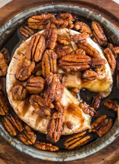 Brown sugar baked brie topped with brown sugar brandy pecans with a slice missing.