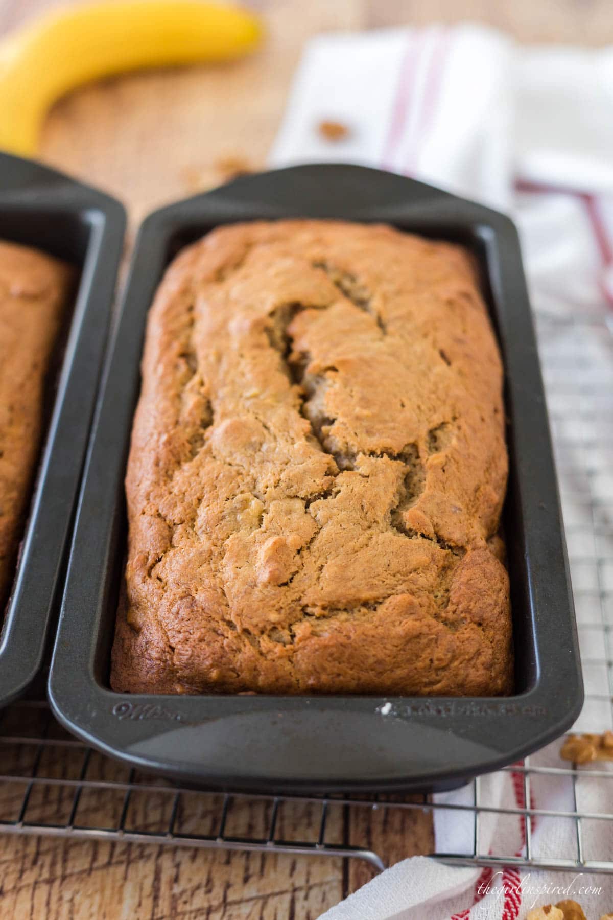 banana nut bread loaves in pan on cooling rack, with banana peel and tea towel