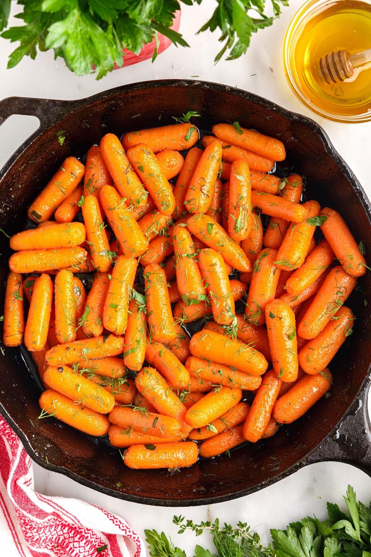 a cast iron skillet with brown sugar honey glazed carrots next to a cup of honey
