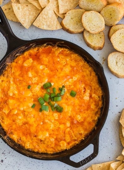 overhead photo of baked buffalo chicken dip with green onions on top, chips and toasted baguette slices, celery sticks
