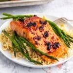 Filet of cherry chipotle glazed salmon plated with roasted asparagus and rice pilaf.
