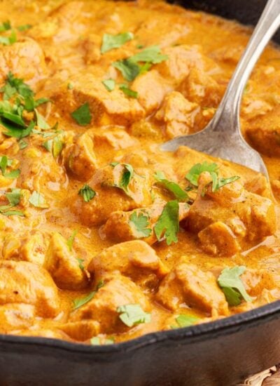 Close up of a skillet of Curry Chicken with a serving spoon inserted.