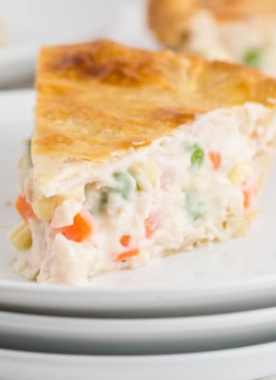 a slice of chicken pot pie on a stack of white serving plates with whole chicken pot pie in the background