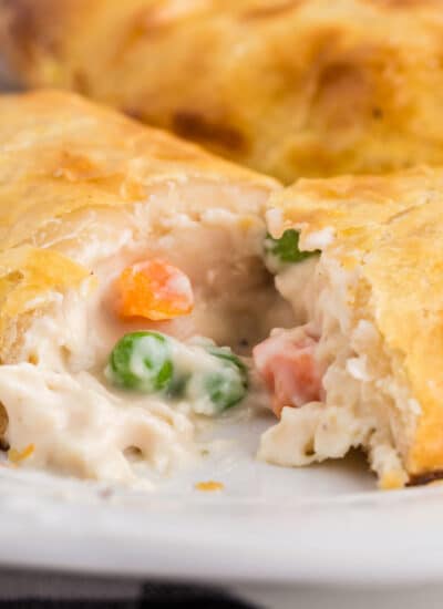 Chicken Pot Pie hand pie cut in half with filling coming out, atop a white serving plate with a tray of baked pies in the background.