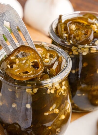 Close up of two jars of Candied Jalapeños with a fork inserted.