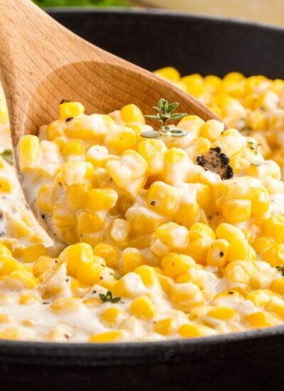 Old Fashioned Creamed Corn with a wooden spoon scooping from the skillet.