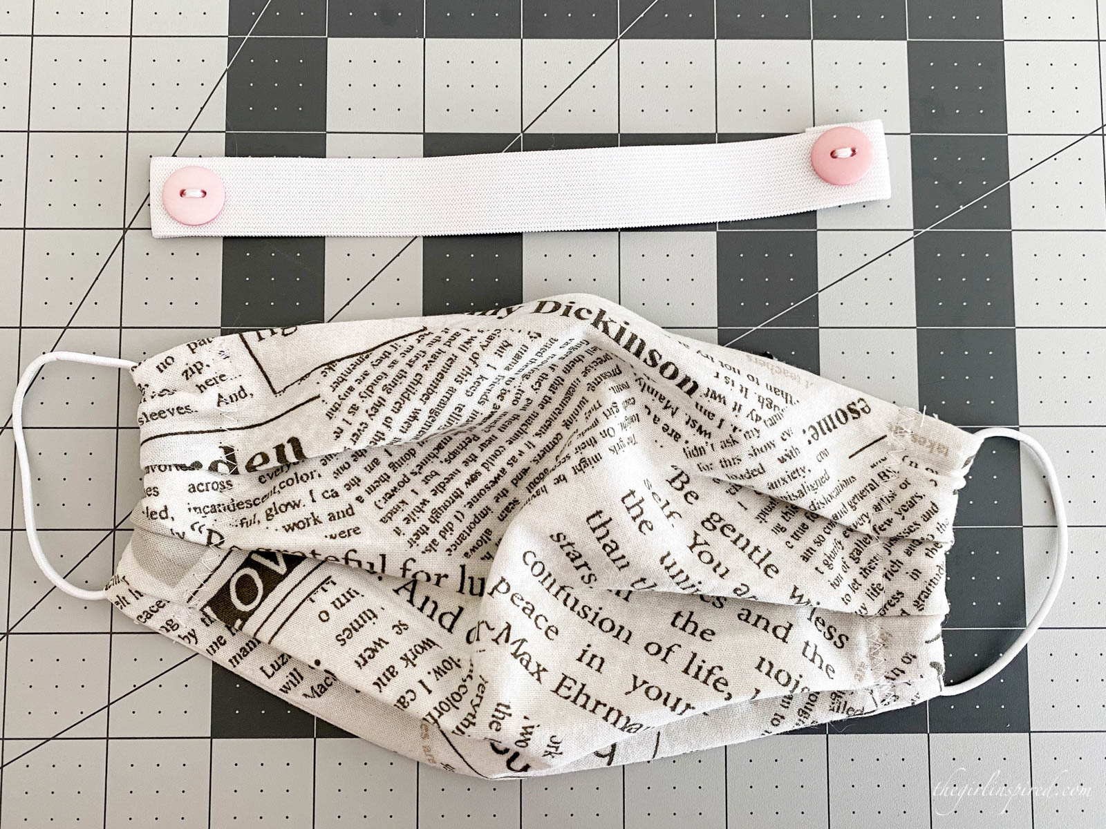 newsprint patterned face mask and white elastic band with pink buttons