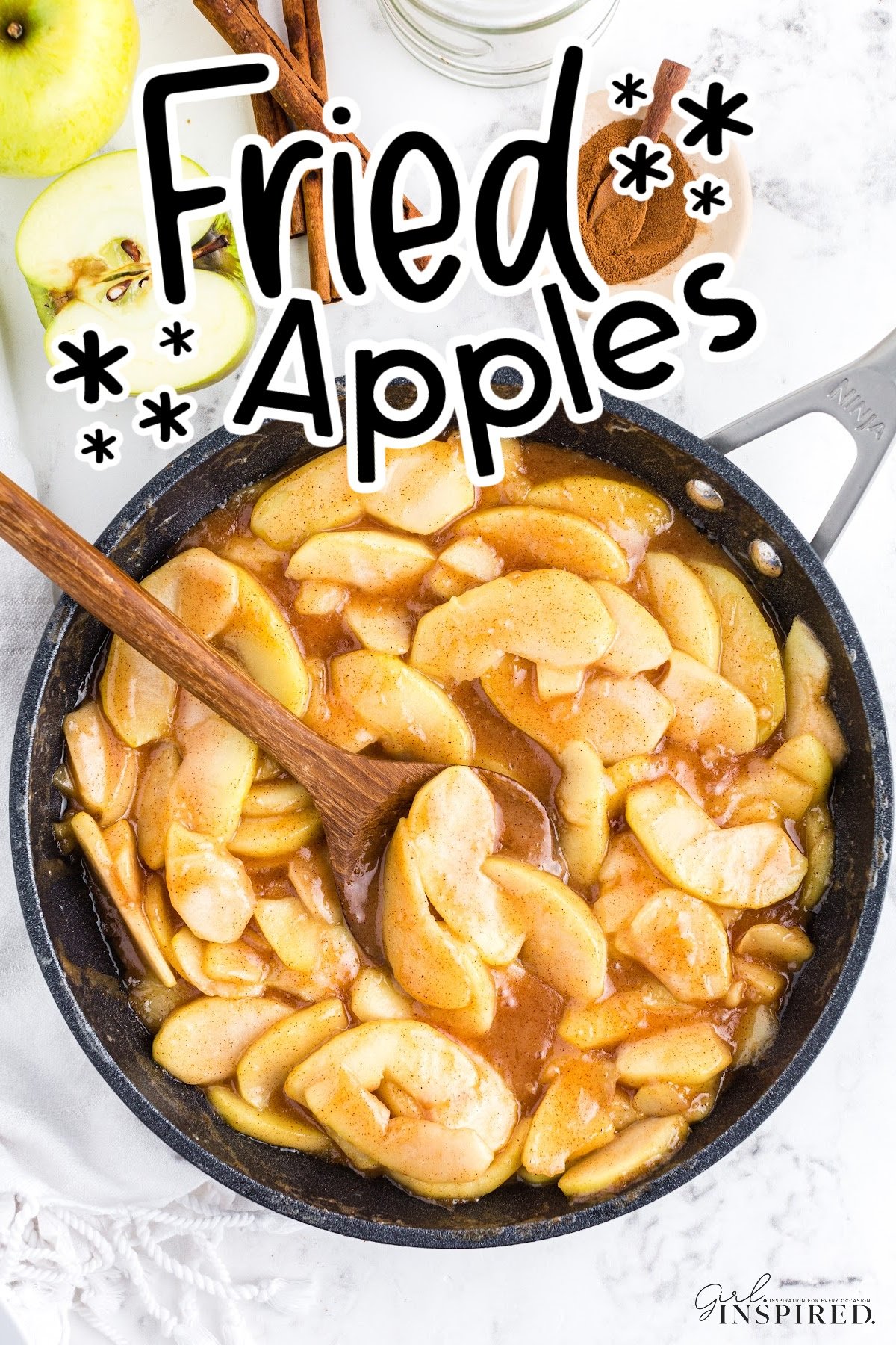 Skillet of fried apples with wooden serving spoon and fresh apple and spices on the side.
