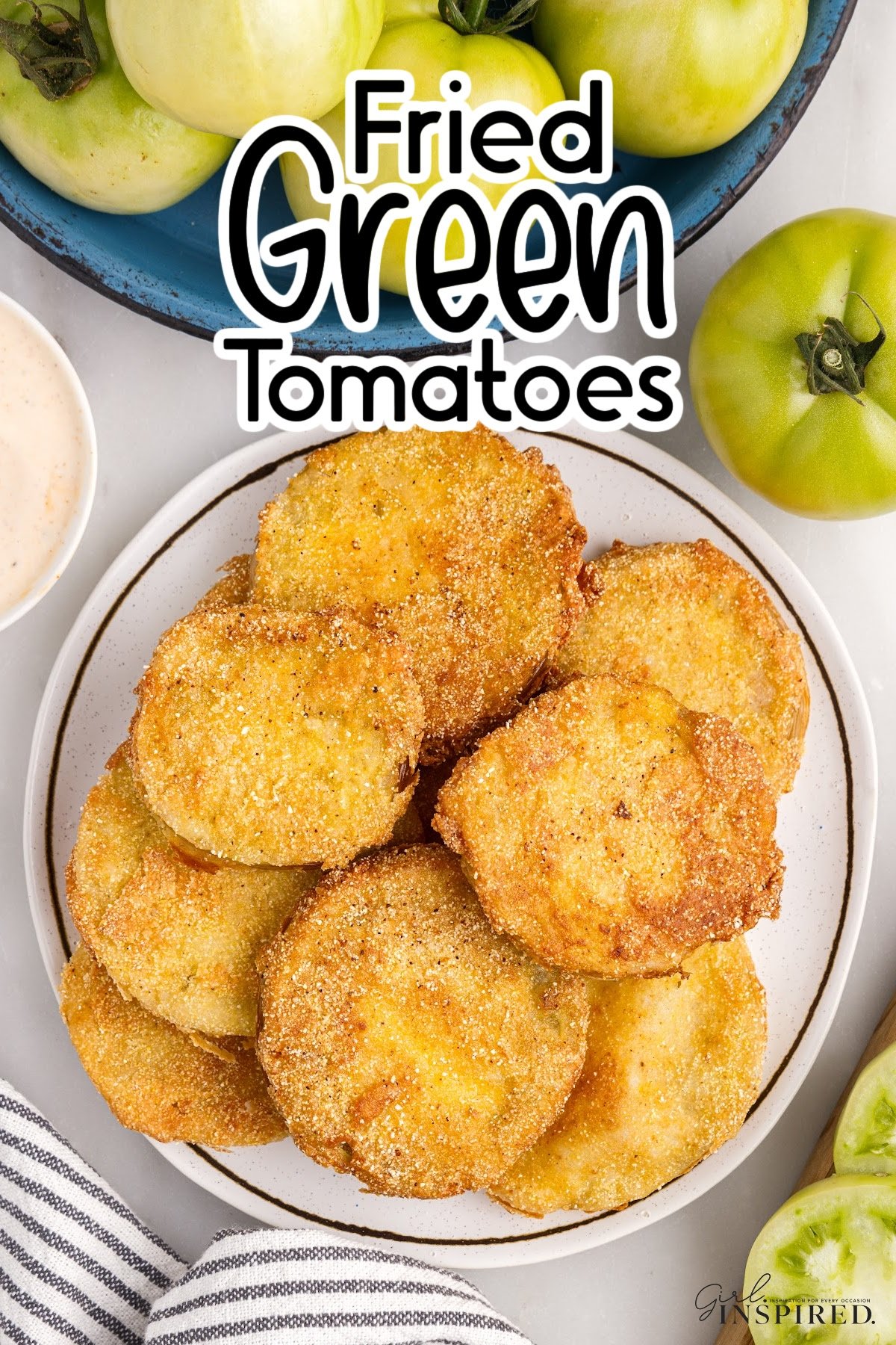 Fried green tomatoes stacked on a platter with whole green tomatoes in a bowl alongside, with text overlay.