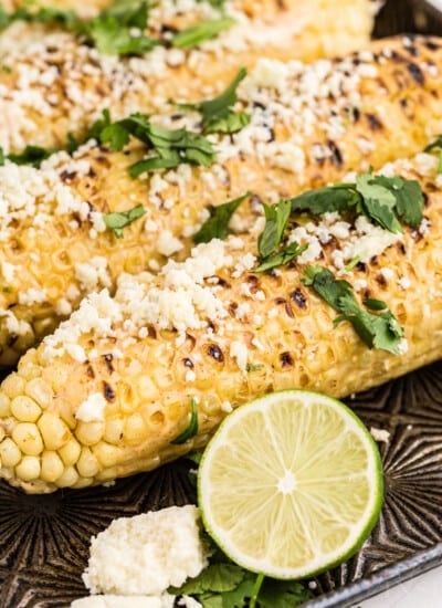 Grilled Mexican Street Corn with cilantro and crumbled cheese garnish, on baking sheet, limes on side