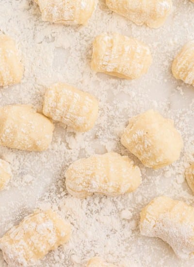 Close up of homemade gnocchi on a marble surface, loose flour in the background.