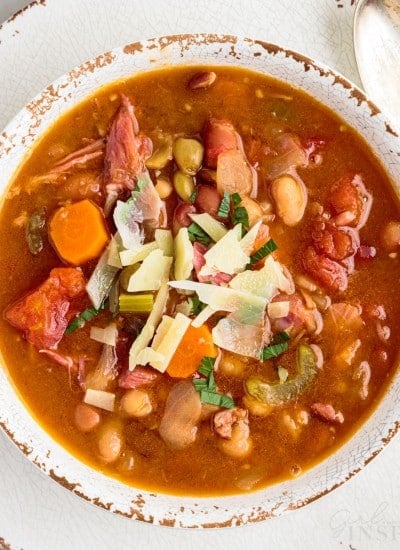 top view close up of 15 bean soup sprinkled with shreds of cheese in a bowl next to a spoon