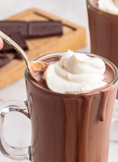 Glass mug of Italian hot chocolate topped with whipped cream with a spoon in it.