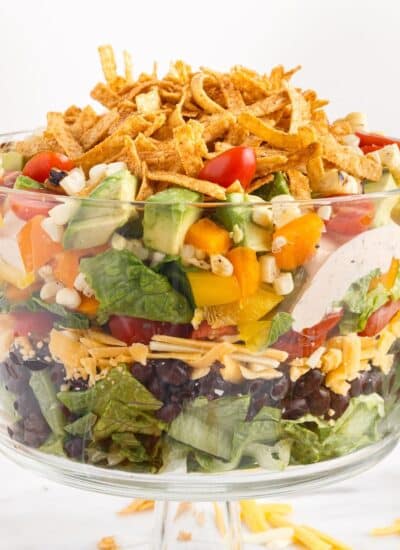 Layered Mexican salad topped with tortilla strips in a trifle bowl.