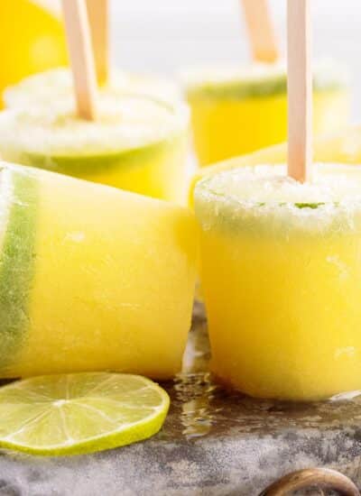 Margarita Popsicles standing on metal ice pack next to fresh lime wheels.