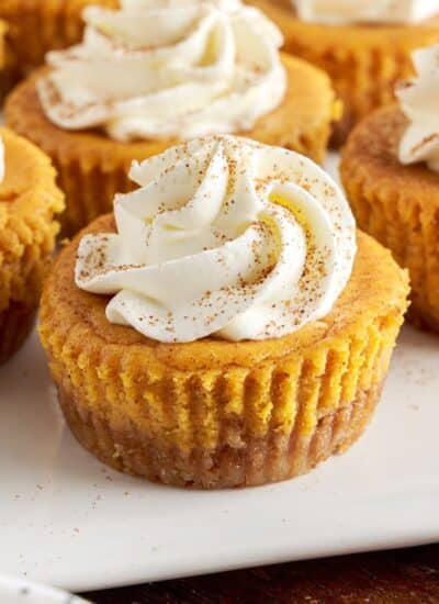 Mini pumpkin cheesecakes on white serving platter, topped with whipped cream.