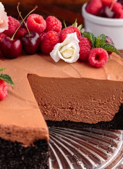 Slices missing from a No Bake Chocolate Cheesecake topped with flowers, cherries, and raspberries.