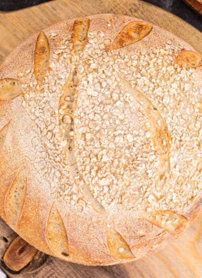 Freshly baked oat sourdough bread on a wooden kitchen board.