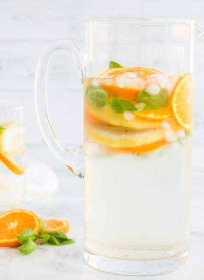 orange slices, lemon slices, and basil leaves with ice and water in glass pitcher and water glasses