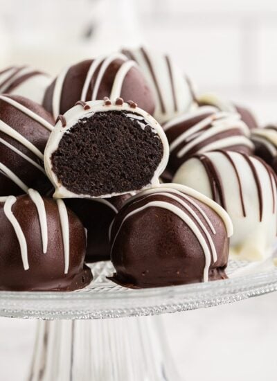 Oreo cookie balls piled on top of each other on a glass cake stand, single Oreo ball cut in half.