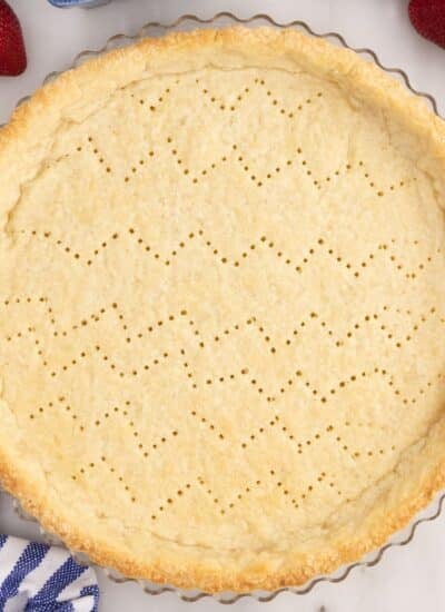 Golden brown Pate Sucree in tart pan on countertop with a few berries and a linen.
