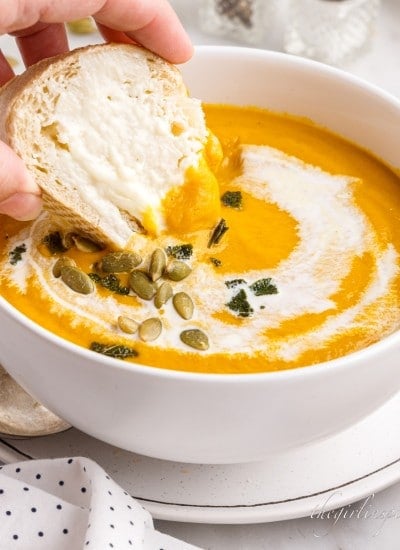 Close up of dipping a piece of bread into pumpkin soup topped with pepitas