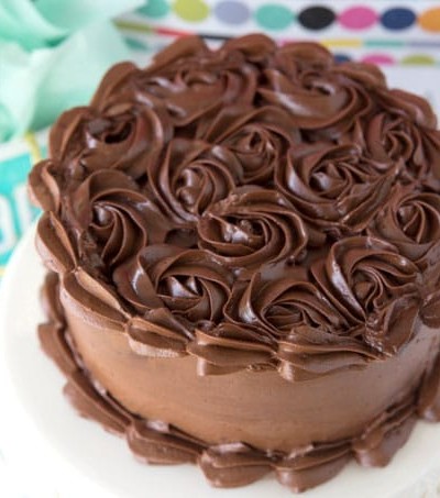 dark chocolate frosting piped in swirls on cake on white platter with birthday gift bags in background