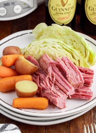 Platter of Slow Cooker Corned beef and cabbage with bottles of Guinness in the background.