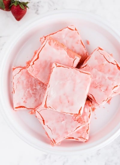 strawberry brownies on white cake plate with bowl of strawberries