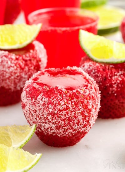 Strawberry daquiri jello shots set on white counter with sugar coating and lime wedges as garnish.