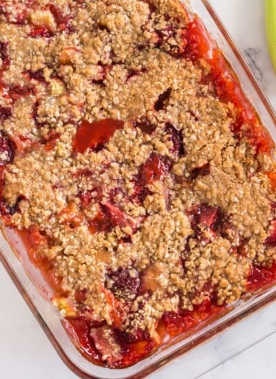 Baked Strawberry Rhubarb Crisp in glass dish with fresh strawberries and rhubarb and red and white linen.